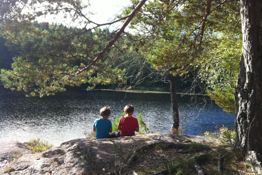 Illustrasjonsfoto - to barn som sitter med ryggen til og ser utover vannet