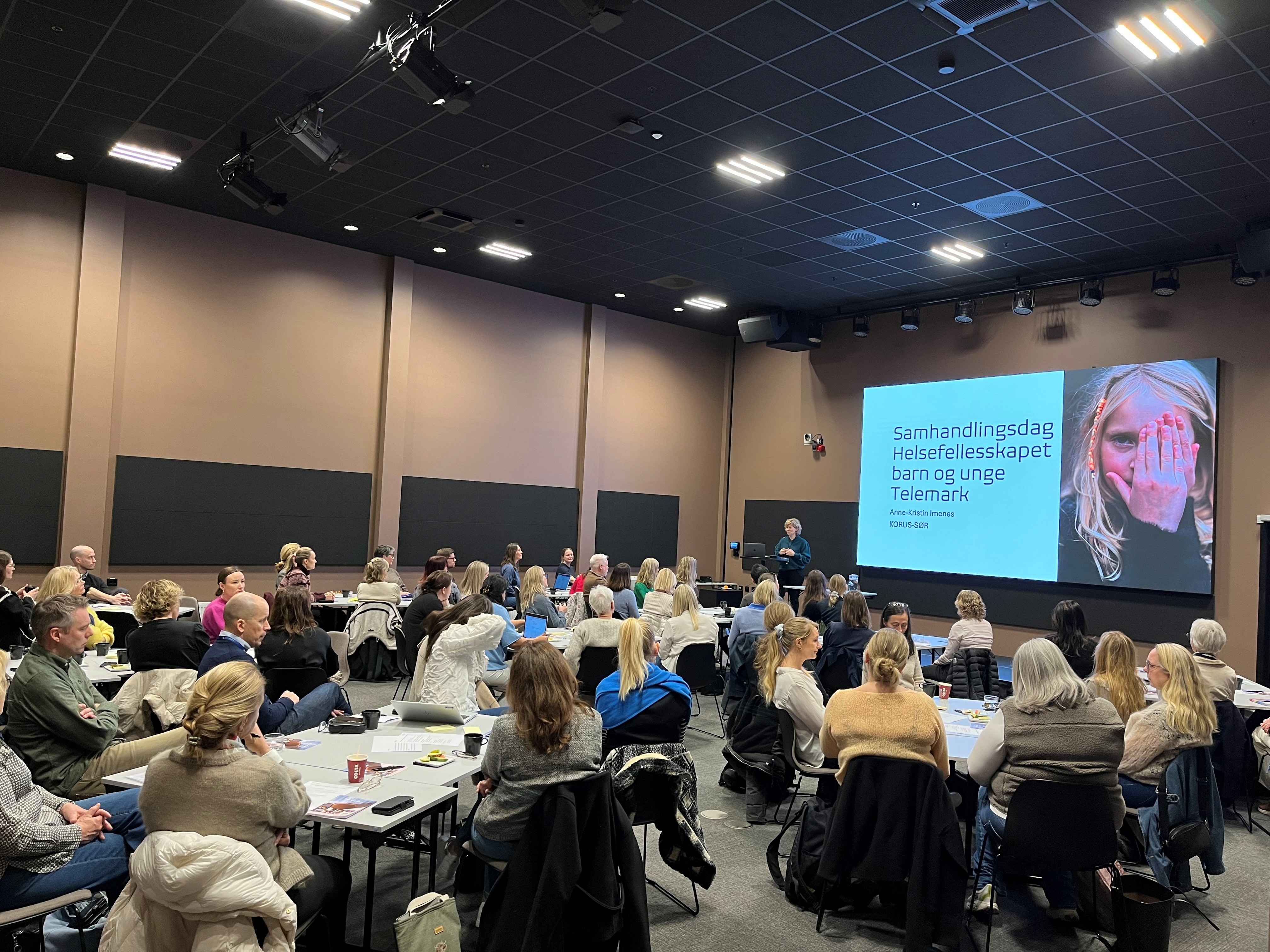 En gruppe mennesker som sitter i et rom og ser på en skjerm