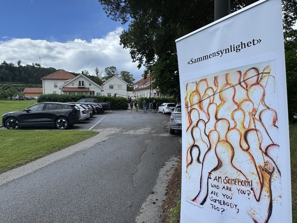 En plakat hvor det står sammensynlighet på, med bygg 10 i bakgrunn