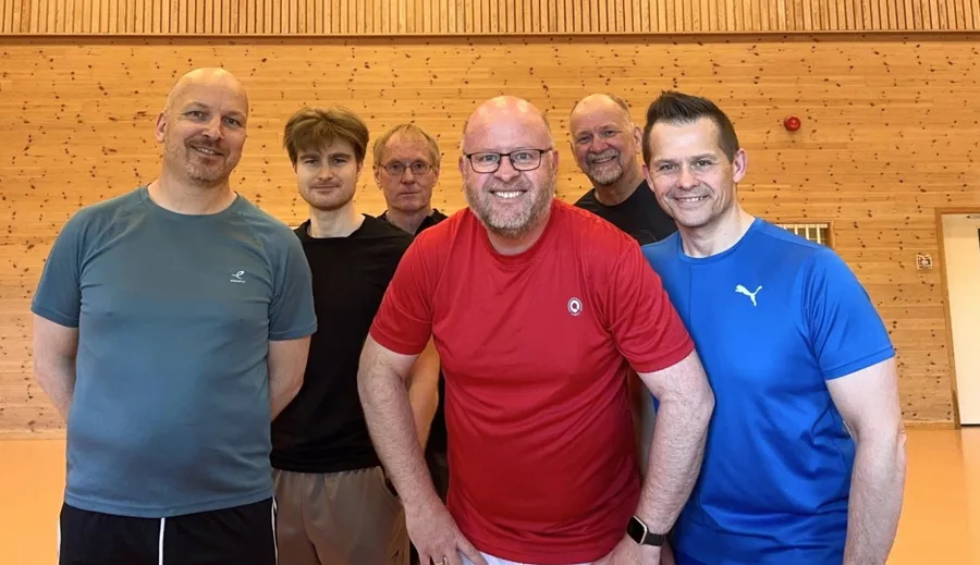 Seks av de ansatte ved sykehuset smiler til kamera og står i en gymsal
