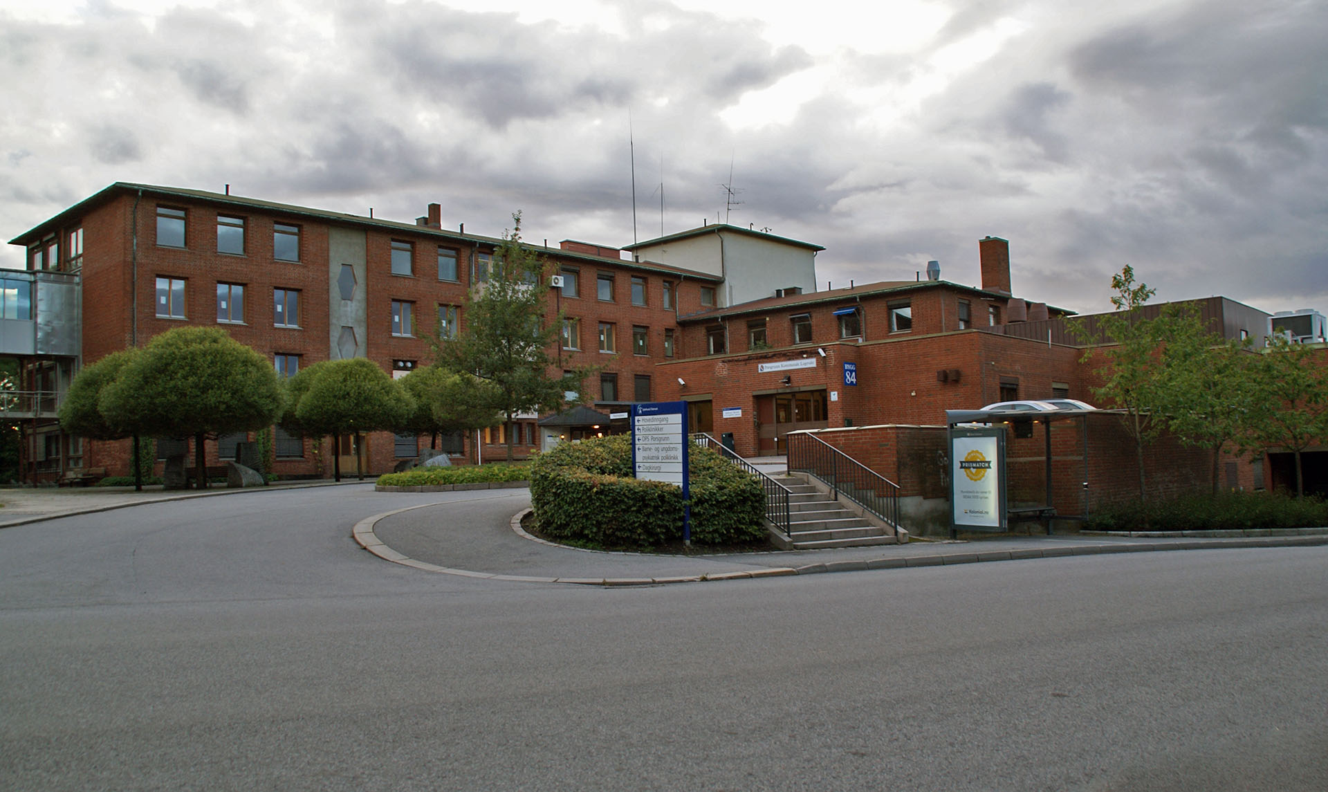 Hovedinngangen til sykehusbygning i Porsgrunn i rød teglstein, med adkomstvei, trapper og informasjonsskilt foran bygget.