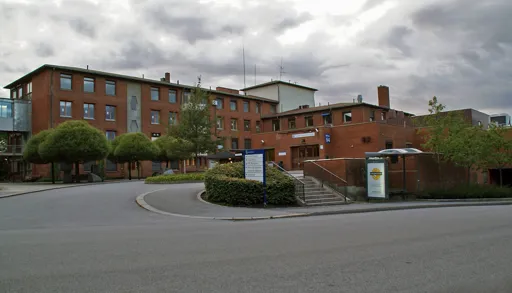 Hovedinngangen til sykehusbygning i Porsgrunn i rød teglstein, med adkomstvei, trapper og informasjonsskilt foran bygget.