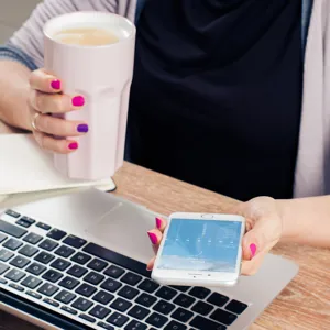 En person som holder en kopp og en mobiltelefon