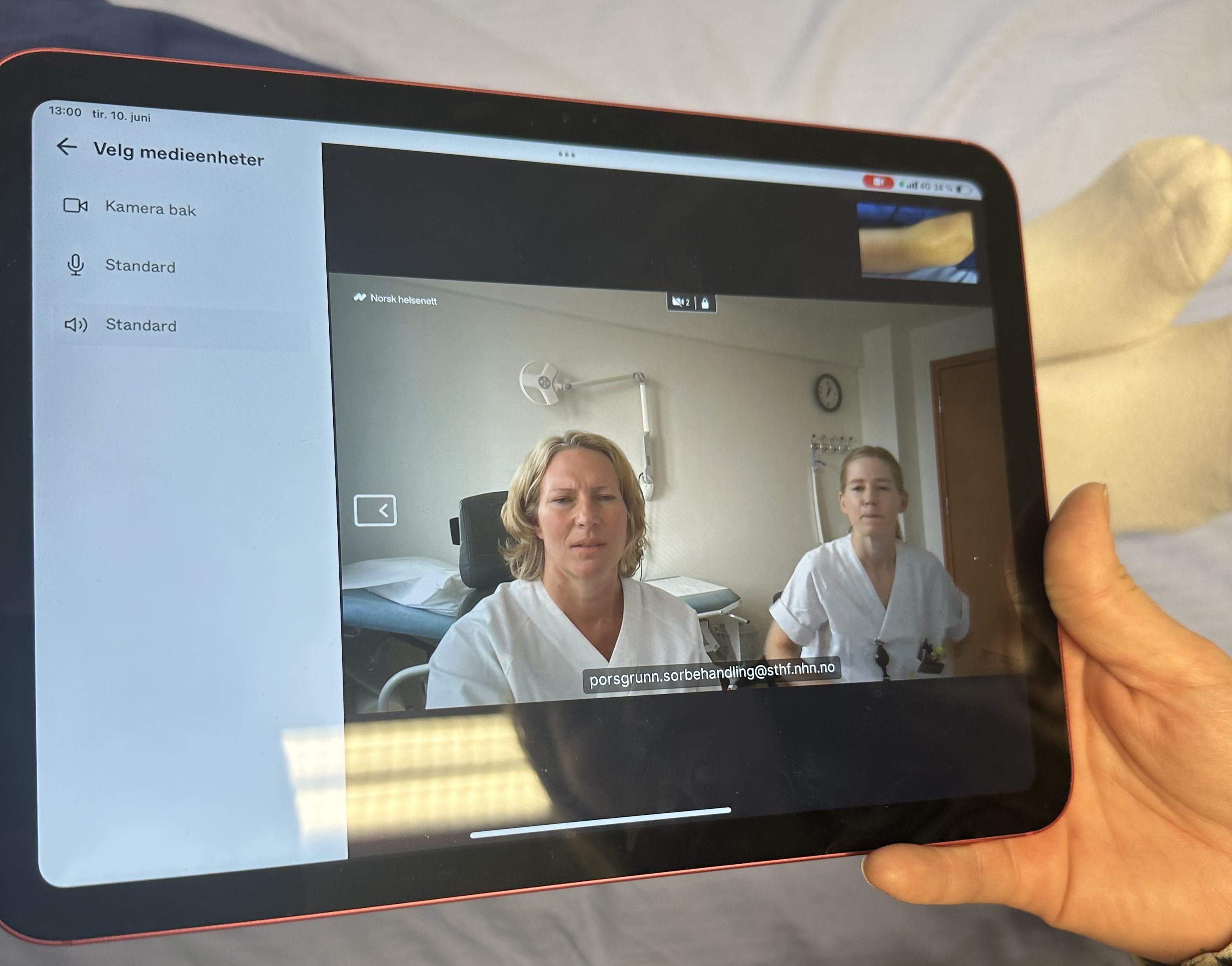 En person som holder en ipad, hvor sårbehandlingen foregår. På ipaden ser man to fra sykehuset.